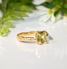 Show your love with this exquisite Peridot ring. Handcrafted in wax and cast in Solid 14k Gold, this stunning green crystal ring features an organic textured band, ensuring its uniqueness. Adorned with a mesmerizing princess-cut Peridot, also the August birthstone, it embodies more than an engagement ring - it symbolizes timeless love and individualityT H E ∙ S M A L L ∙ D E T A I L S• Princess-cut Peridot (5 x 5mm)• Solid 14k Gold textured bandM A T E R I A L ∙ O P T I O N S• Sterling Silver• S Peridot And Diamond Engagement Rings, Organic Gold Engagement Ring, Gold Emerald Ring With Nature-inspired Design, Nature-inspired Rings With May Birthstone Gemstone, Nature-inspired Gemstone Rings For May Birthstone, Nature-inspired Rings With May Birthstone, Fine Jewelry Peridot Rings For May Birthstone, Peridot Engagement Rings Gold, Unique Peridot Jewelry For May Birthstone