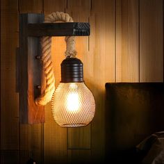 a light bulb hanging from a rope on a wall next to a bed with a wooden headboard