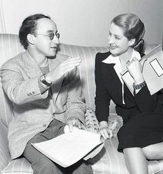 an old black and white photo of two people sitting on a couch talking to each other