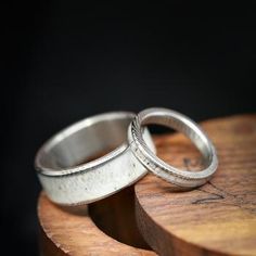 two silver wedding rings sitting on top of a wooden table next to each other with black background