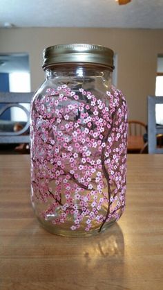 a glass jar with pink flowers painted on it sitting on top of a wooden table