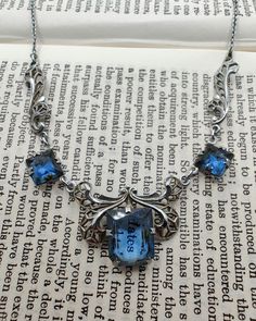 Gorgeous vintage Art Deco necklace with open back blue glass set in chrome filigree. The blue glass is a vibrant sapphire colour and the setting reminds me of a butterfly, which I think is uniquely lovely. There is also a mark on the clasp ring but I can't make it out. In very good vintage condition with some wear to the chrome finish (please see photos), and could use a thorough clean by someone who knows what they're doing. The necklace is 41cm long and the centre stone measures 1.1cm by 0.9cm Ornate Blue Nickel-free Jewelry, Ornate Nickel-free Blue Jewelry, Blue Victorian Jewelry For Collectible, Antique Blue Sterling Silver Jewelry, Antique Blue Metal Jewelry, Antique Nickel-free Blue Jewelry, Antique Blue Nickel-free Jewelry, Victorian Blue Jewelry For Collectors, Antique Blue Gemstone Necklaces