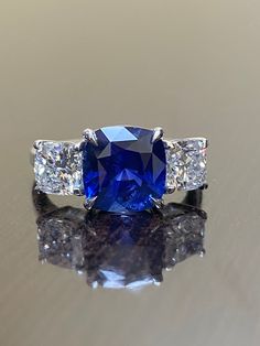 "DeKara Designs Collection Beautiful Modern/Art Deco Ceylon Blue Sapphire and Diamond Ring Metal- 90% Platinum, 10% Iridium Stones- Genuine Ceylon Cushion Cut Blue Sapphire 4.14 Carats. Two GIA Certified Cushion Cut Diamonds E Color VS2 0.92 Carats, F Color SI1 Clarity 0.95 Carats. Ring Comes With Sapphire Certificate and GIA Diamond Certificates. Size-7. FREE SIZING Entirely Handmade, Classic and Timeless Art Deco Inspired Ceylon Blue Sapphire Three Stone Cushion Cut Diamond Engagement Ring. Th Blue Sapphire Ring With Diamond Cut Asscher Shape, Gia Certified Blue Sapphire Ring In Platinum, Blue Asscher Cut Diamond Sapphire Ring, Cushion Cut Blue Sapphire Rings, Blue Asscher Cut Sapphire Ring With Diamond Details, Blue Asscher Cut Sapphire Ring With Diamond Cut, Blue Cushion Cut Lab-created Sapphire Rings, Luxury Blue Diamond Anniversary Ring, Sapphire Rings With Diamond Cushion Cut