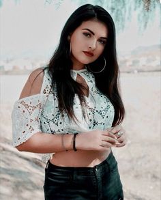 a woman with long dark hair wearing a white top and black pants is posing for the camera