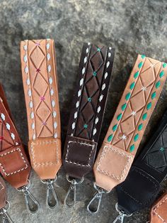 five different colored leather key chains are lined up on a stone surface with metal hooks