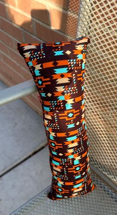 an orange and blue patterned pillow sitting on top of a metal bench next to a brick wall