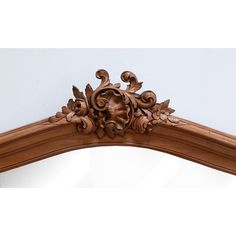 an ornate wooden mirror frame with carved leaves and flowers on the top, against a white wall