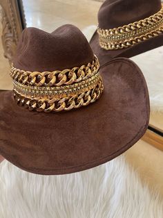 Our love of hats just got became a full-on obsession: meet the Beth Dutton Chain Banded cowboy hat! The most chic, high-end hat we could've ever dreamed up. A hat this good needs to be worn as much as possible and with every single outfit! Hand made by artisans, incredible quality, pure suede, hand placed chain around the crown, too many details to list! The best part? It's super structured with an elastic band on the inside that will fit EVERYONE. Btw never taking this hat off. These hats are a Gold Wide Brim Fedora For Festivals, Western Gold Fedora With Short Brim, Western Style Gold Fedora With Flat Brim, Western Style Gold Fedora With Short Brim, Luxury Fedora For Kentucky Derby And Rodeo, Luxury Adjustable Hat For Country Events, Luxury Fedora For Rodeo And Kentucky Derby, Luxury Wide Brim Hats For Country Events, Brown Western Fedora For Party