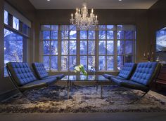 a living room filled with furniture and a chandelier above a glass table surrounded by windows