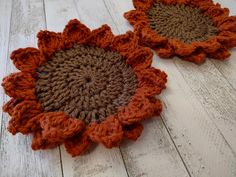 two crocheted sunflowers sitting on top of a white wooden floor next to each other