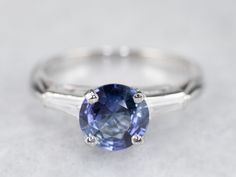 This vintage sapphire and diamond engagement ring is the epitome of a classic! This intense blue sapphire is a perfect, rich color, the benchmark for a fine sapphire. The crisp blue hue is filled with glitter and it has phenomenal light refraction, depth of color, and sparkle on the finger! We've set this in a tasteful platinum mounting featuring baguette diamonds on either side, equal in quality and sparkle to this lovely center sapphire. The ring was originally designed as an engagement piece, Classic Gia Certified Sapphire Ring, Classic Blue Sapphire Ring In Platinum, Timeless Baguette-cut Sapphire Ring, Timeless Blue Sapphire Ring Gia Certified, Timeless Round Cut Sapphire Ring, Timeless Gia Certified Blue Sapphire Ring, Classic Sapphire Tanzanite Solitaire Ring, Classic Tanzanite Solitaire Sapphire Ring, Timeless Sapphire Ring In Platinum