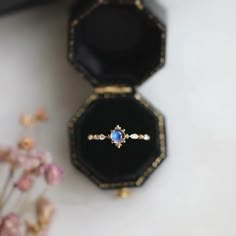 an open ring box sitting on top of a table next to a flower vase and some flowers