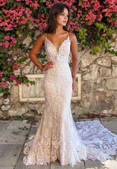 a woman standing in front of flowers wearing a wedding dress with an open back and spaghetti straps