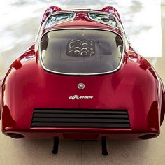 the front end of a red sports car with its hood up and lights on, from above