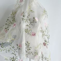 a white scarf with pink and green flowers hanging on a clothes rack in front of a white wall