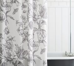 a bath tub sitting next to a shower curtain with flowers on it and a white wall behind it