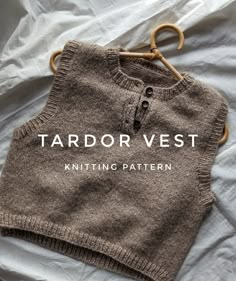 a knitted vest sitting on top of a bed next to a wooden hanger