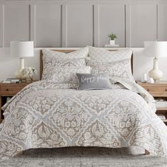 a white and beige comforter set on a bed with two lamps next to it