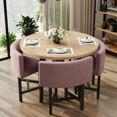 a dining room table with pink chairs and plates on the wooden floor next to a window