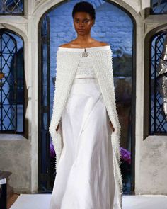 a model walks down the runway in a white gown with an off - shoulder cape