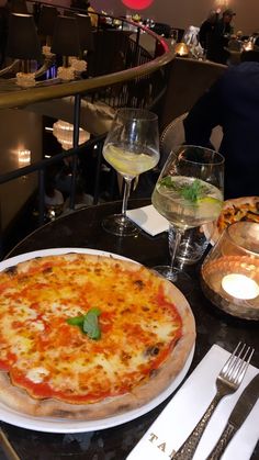 a pizza sitting on top of a white plate next to glasses of wine and silverware