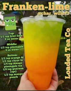 a hand holding up a drink with orange and green liquid in it's cup