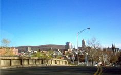 an empty street in front of a city with tall buildings on the hill behind it