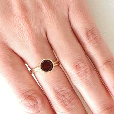 a woman's hand wearing a gold ring with a red stone on the middle