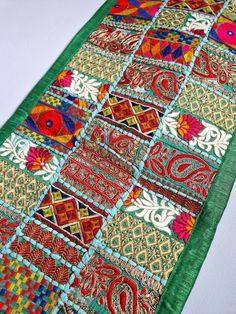 a green table runner with red, yellow and blue designs on the border is laying on a white surface