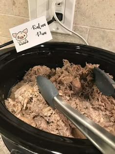 a slow cooker filled with shredded meat next to a sign that reads kilnu pan