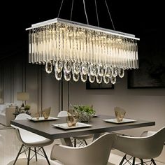 a chandelier hanging over a dining room table with white chairs and plates on it