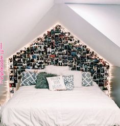 a white bed topped with lots of pictures under a slanted ceiling next to a window