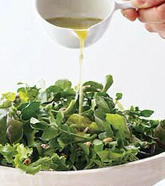 a person pouring dressing into a salad in a white bowl on top of a table