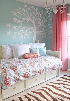 a bedroom decorated in blue and pink with a tree painted on the wall above the bed