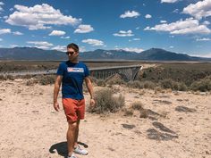 a man standing on top of a dirt field next to a desert area with mountains in the background