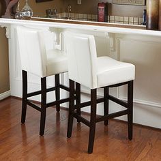 two white bar stools sitting in front of a counter