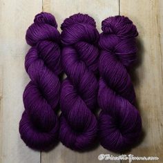 three skeins of purple yarn sitting on top of a wooden floor