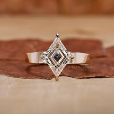 a diamond ring sitting on top of a piece of brown paper next to a leaf