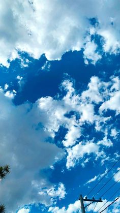 the sky is filled with clouds and power lines in front of palm trees on a sunny day