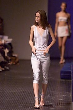 a woman is walking down the runway at a fashion show wearing silver pants and a white tank top