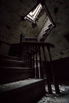 an abandoned staircase with light coming in from the top and dark lighting at the bottom