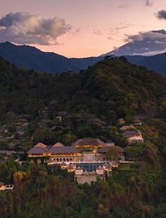 an aerial view of a resort surrounded by trees and mountains at dusk with the sun setting