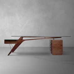 a desk with a glass top and wooden structure on the bottom, in front of a concrete wall