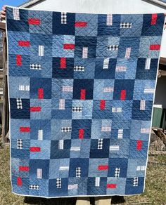 a blue and red quilt hanging from a clothes line in front of a white house