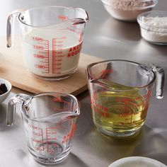 measuring cups filled with liquid on top of a wooden cutting board next to other ingredients