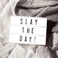 a sign that says slay the day on it sitting on top of a bed