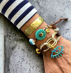 Elevate your accessory game with this stunning boho chic bracelet set. Featuring a blend of turquoise and gold tones, this set includes a handmade adjustable cord bracelet adorned with turquoise donuts and evil eye charms, paired with a hammered brass cuff. Perfect for adding a touch of bohemian elegance to any outfit. Ideal for summer fashion, festival wear, and unique gift ideas for her. Bohemian Cuff Bracelet Bangle For Beach, Bohemian Beach Cuff Bracelet Bangle, Bohemian Bangle Cuff Bracelet For The Beach, Bohemian Cuff Bangle For Beach, Hippie Gold Bracelets For Festivals, Turquoise Hand Wrapped Bracelets For Festivals, Bohemian Resizable Bangle Cuff Bracelet, Gold Bohemian Evil Eye Bracelet For Festival, Adjustable Bohemian Brass Bracelets