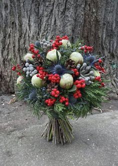 a bouquet of berries, pine cones and other greenery sits in front of a tree