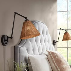 a bed with two lamps on the headboard next to pillows and a potted plant