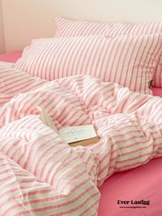 a pink and white striped bed spread with a book on the pillowcase in front of it